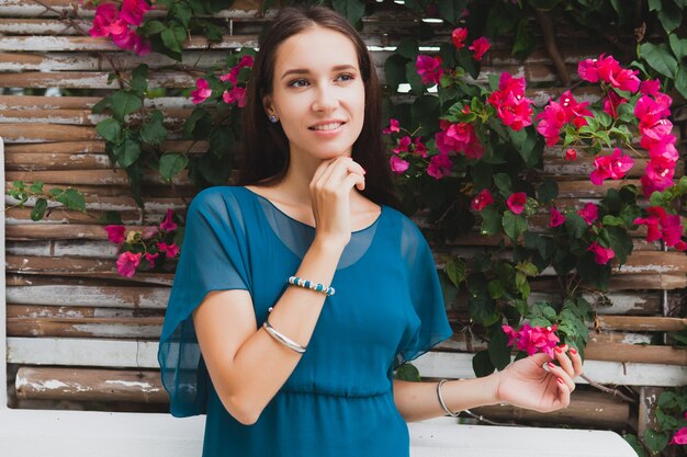 Junge stilvolle schöne Frau im blauen Kleid, Sommermodetrend, Urlaub, Garten, tropische Hotelterrasse, lächelnd