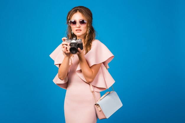 Junge stilvolle sexy Frau im rosa Luxuskleid, Sommermodetrend, schicker Stil, Sonnenbrille, Fotografieren auf Vintage-Kamera