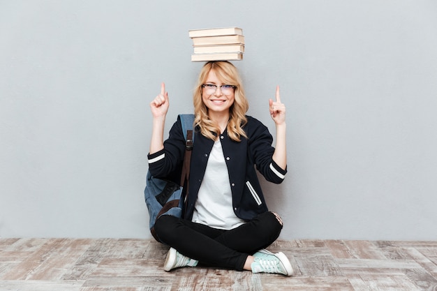 Junge studentin, die bücher auf kopf hält und zeigt