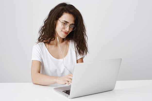 Junge Studentin, die mit Laptop arbeitet und an Anzeige lächelt