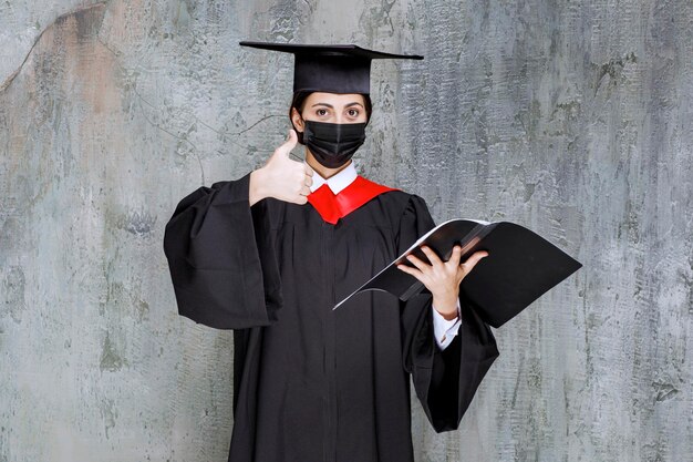 Junge Studentin mit schwarzer Maske verhindert die Verbreitung von Viren bei ihrer Abschlussrede. Foto in hoher Qualität