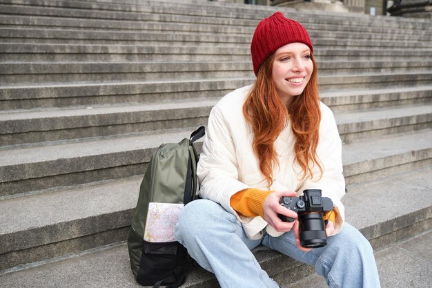 Junge studentische Fotografin sitzt auf Straßentreppen und überprüft ihre Aufnahmen auf professioneller Kameraaufnahme