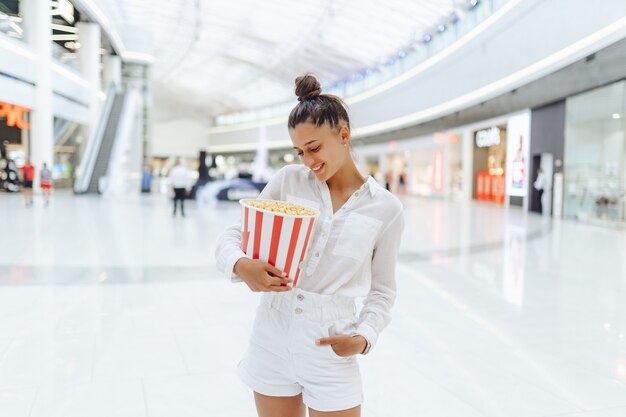 junge süße Frau, die Popcorn im Einkaufszentrumhintergrund hält