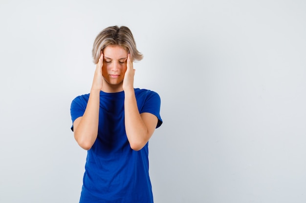 Junge Teenager, die an Migräne im blauen T-Shirt leiden und beunruhigt aussehen. Vorderansicht.