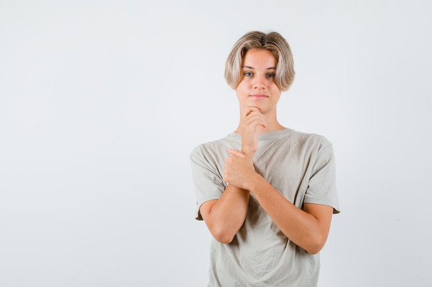 Junge Teenager, die das Kinn im T-Shirt stützen und positiv aussehen. Vorderansicht.