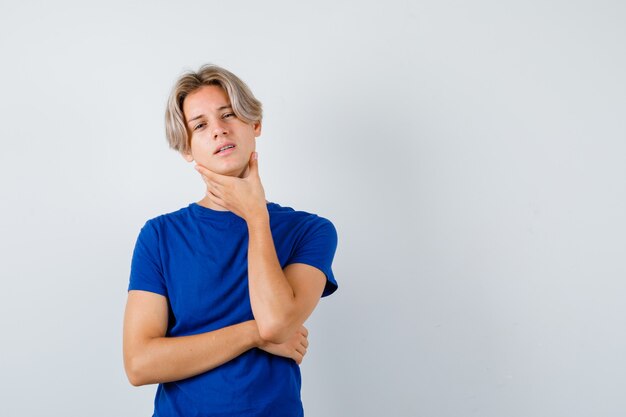 Junge Teenager, die Halsschmerzen im blauen T-Shirt haben und krank aussehen, Vorderansicht.