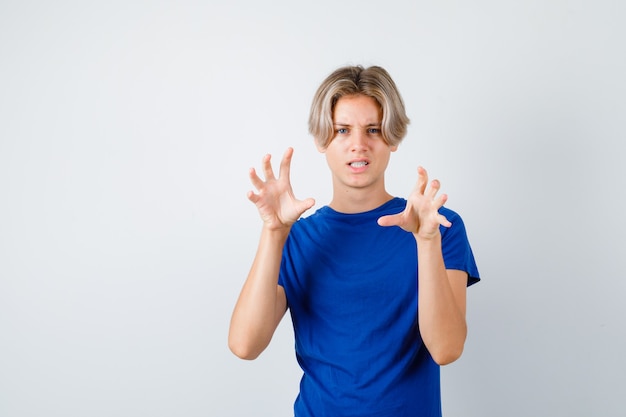 Junge Teenager, die Krallen zeigen, die eine Katze im blauen T-Shirt imitieren und aggressiv aussehen, Vorderansicht.