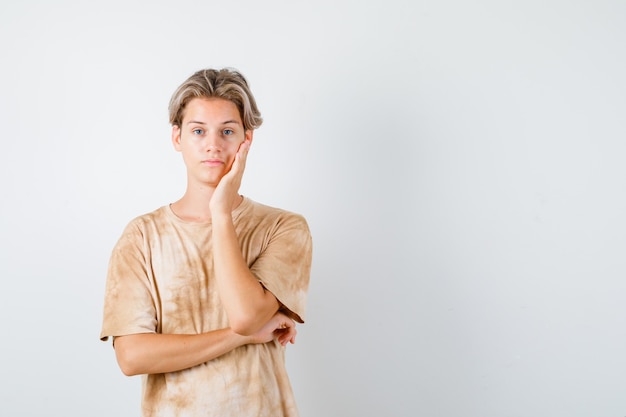 Junge Teenager, die sich im T-Shirt auf die Handfläche lehnen und enttäuscht aussehen, Vorderansicht.