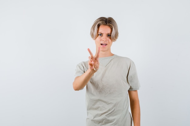 Junge Teenager, die Siegesgeste im T-Shirt zeigen und selbstbewusst aussehen, Vorderansicht.