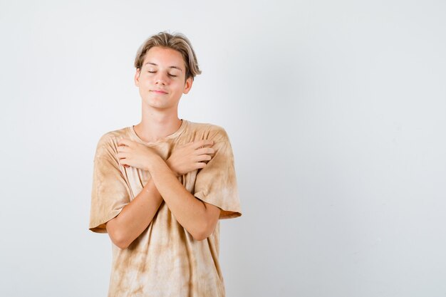 Junge Teenager, die verschränkte Arme auf der Brust halten, die Augen im T-Shirt schließen und friedlich aussehen. Vorderansicht.