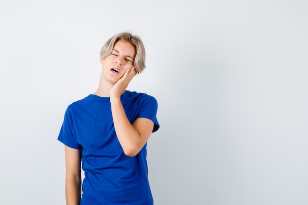 Junge Teenager im blauen T-Shirt, die unter schrecklichen Zahnschmerzen leiden und belästigt aussehen, Vorderansicht.