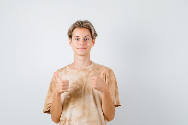 Junge Teenager im T-Shirt, die doppelte Daumen nach oben zeigen und lustig aussehen, Vorderansicht.