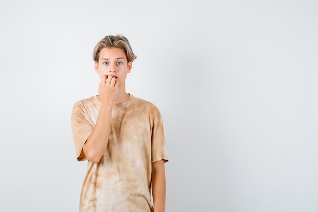 Junge Teenager im T-Shirt, die emotional Nägel beißen und ängstlich aussehen, Vorderansicht.