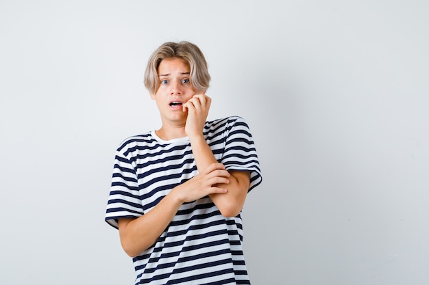 Junge Teenager mit der Hand auf der Wange im gestreiften T-Shirt und erschrocken. Vorderansicht.