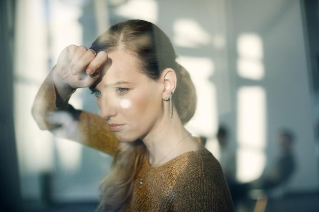 Kostenloses Foto junge traurige frau, die sich an ein fenster lehnt und durch es schaut