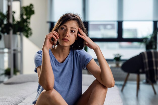 Junge traurige Frau, die über Handy kommuniziert und wegschaut, während sie an etwas denkt