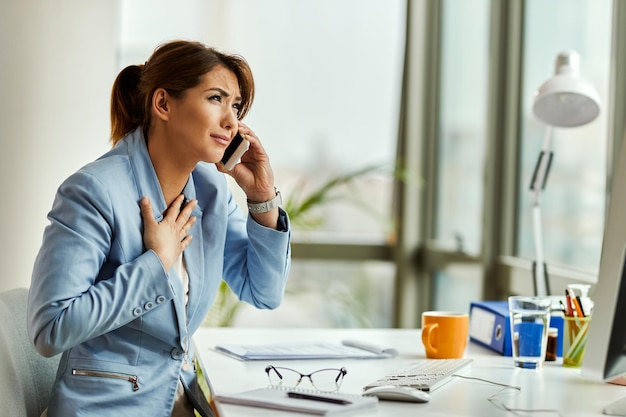 Junge traurige Geschäftsfrau, die schlechte Nachrichten erhält, während sie im Büro mit dem Handy telefoniert