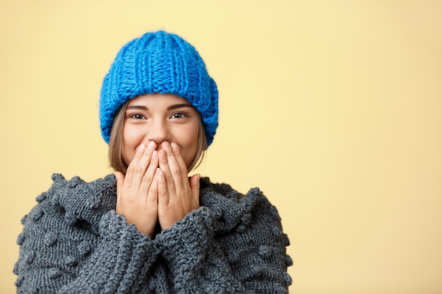 Kostenloses Foto junge überraschte schöne blonde frau in strickmütze und pullover auf gelb.