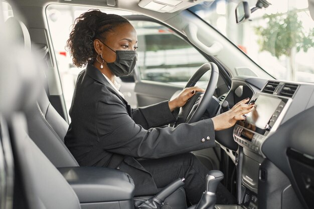 Junge und fröhliche Frau, die ein neues Auto genießt, während sie im Inneren sitzt Schwarze Frau, die ein Auto fährt Mädchen, das schwarzes Kostüm trägt