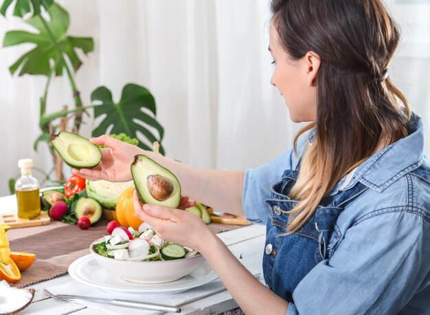 Junge und glückliche Frau, die die Avocado am Esstisch betrachtet