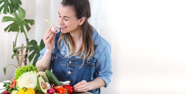 Junge und glückliche Frau, die Salat am Tisch isst, auf einem hellen Hintergrund in Jeanskleidung. Das Konzept eines gesunden hausgemachten Lebensmittels. Platz für Text.