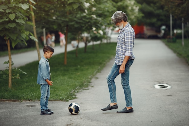 Junge und Großvater gehen im Park spazieren. Alter Mann, der mit Enkel spielt. Familie spielt mit einem Ball.