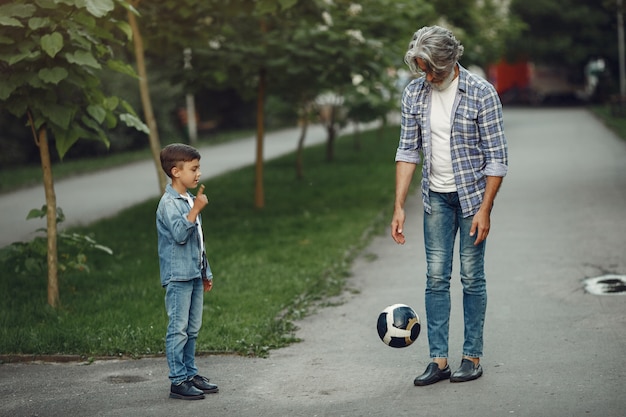 Junge und Großvater gehen im Park spazieren. Alter Mann, der mit Enkel spielt. Familie spielt mit einem Ball.