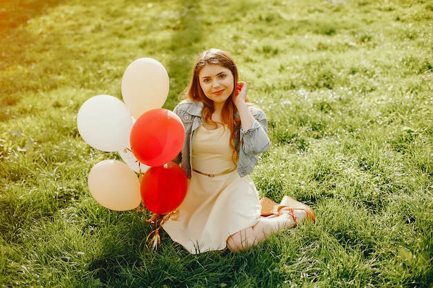 Junge und helle Mädchen, die in den Sommerpark mit Ballonen gehen