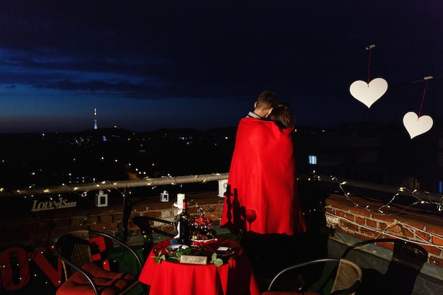 Junge und Mädchen umarmen sich zarte stehend auf der Dachspitze in den Strahlen der Abendlichter