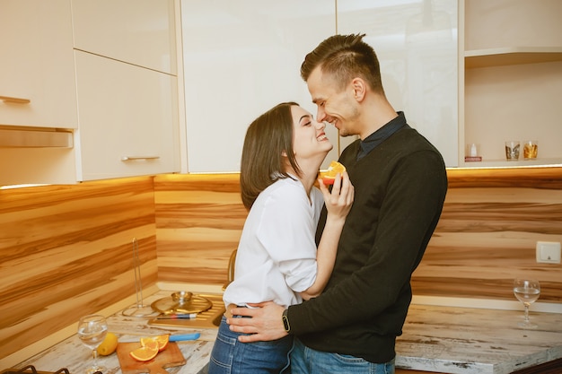 Junge und süße reizende Paare, die in der Küche mit Orange stehen