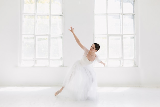 Junge und unglaublich schöne Ballerina posiert und tanzt in einem weißen Studio