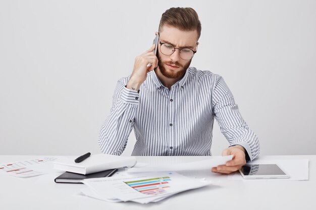 Junge unerfahrene männliche Arbeiter mit Stoppeln verstehen Informationen in Dokumenten oder Papier nicht