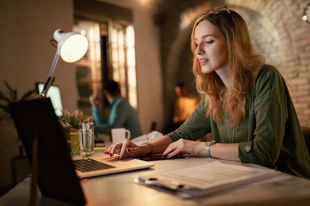 Junge Unternehmerin mit Computer, während sie nachts im Büro arbeitet