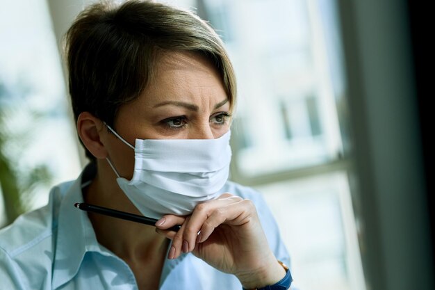 Junge Unternehmerin trägt Gesichtsmaske, während sie in ihrem Büro arbeitet