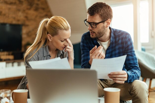 Junge unzufriedene Paare, die sich unterhalten, während sie ihre Hausfinanzen analysieren