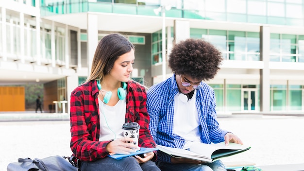 Junge verschiedene Paare, die außerhalb des Collegegebäudes sitzen