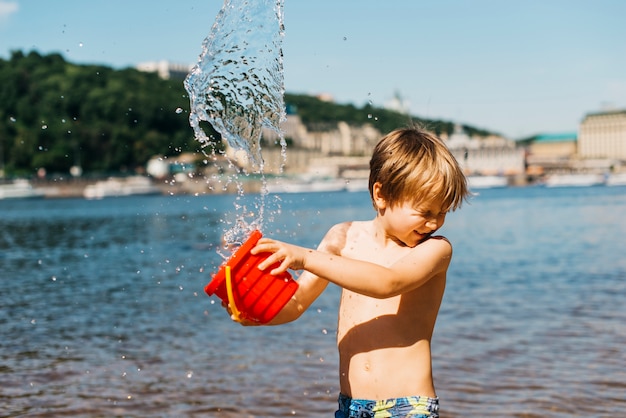 Junge verschüttet Wasser vom Eimer auf Seestrand