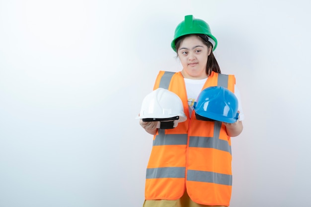 Junge weibliche Bauarbeiterin im Helm, der Helme über weißer Wand hält