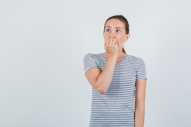 Junge weibliche beißende Faust im gestreiften T-Shirt und suchen ängstlich, Vorderansicht.