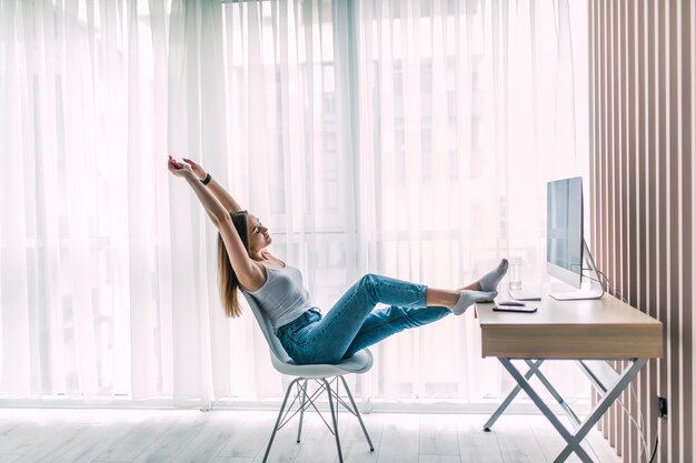Junge weibliche Freiberufler, die sich ausdehnt und entspannt am Laptop im Heimbüro arbeitet