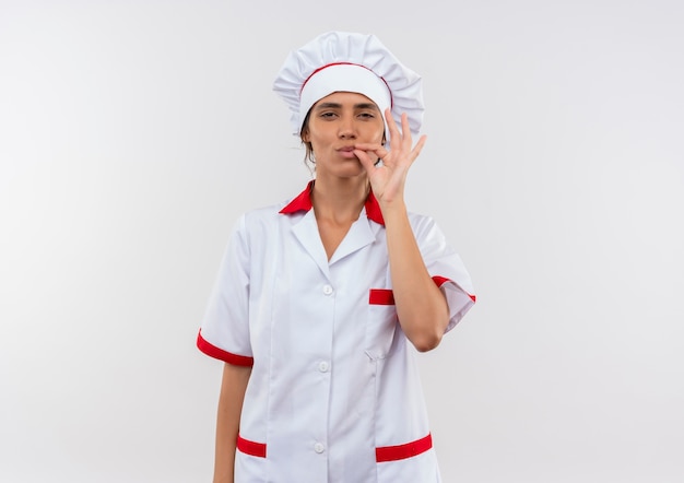 junge weibliche Köchin, die Kochuniform trägt, die köstliche Geste auf isolierter weißer Wand mit Kopienraum zeigt
