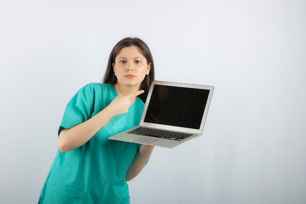 Junge weibliche Krankenschwester, die auf Laptop auf Weiß zeigt.