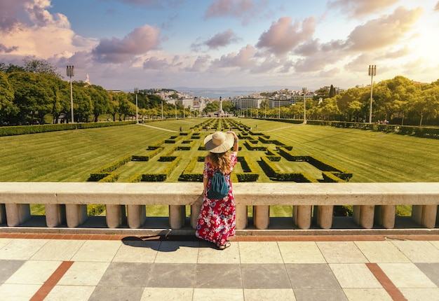 Kostenloses Foto junge weibliche touristen in einem roten blumenkleid im park eduardo vii unter dem sonnenlicht in portugal