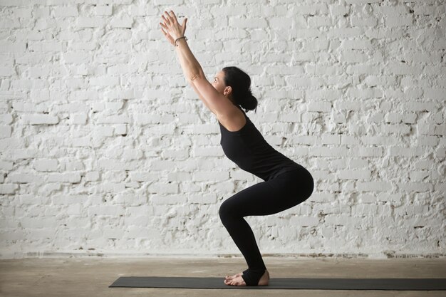 Junge Yogi attraktive Frau in Utkatasana Pose, weiße Loft Backg