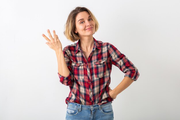 Junge ziemlich lustige emotionale Frau im karierten Hemd, das lokalisiert auf weißer Studiowand aufwirft, zeigt Geste