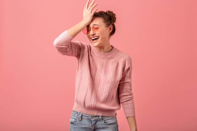 Junge ziemlich lustige emotionale lachende Frau im rosa Pullover und in der Sonnenbrille lokalisiert auf rosa Studiohintergrund