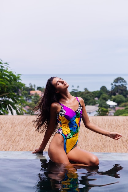 Junge ziemlich positive glückliche schlanke Frau im bunten Badeanzug an der Luxusvilla des erstaunlichen Hotels, das schönen Tag im Urlaub in Thailand genießt