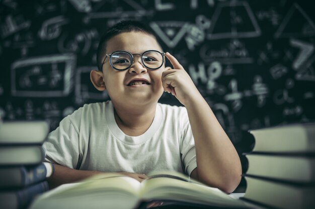 Jungen mit Brille schreiben Bücher und denken im Klassenzimmer