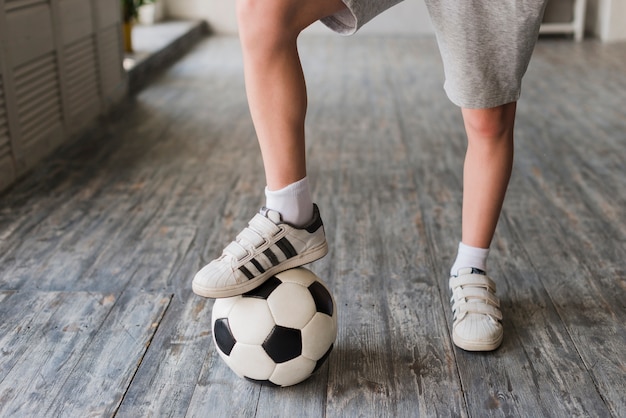 Jungenfuß auf Fußball über dem Massivholzboden