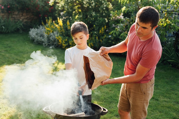 Jungenholdingzange, die mit seinem Vater einsetzt Kohle in Grill steht